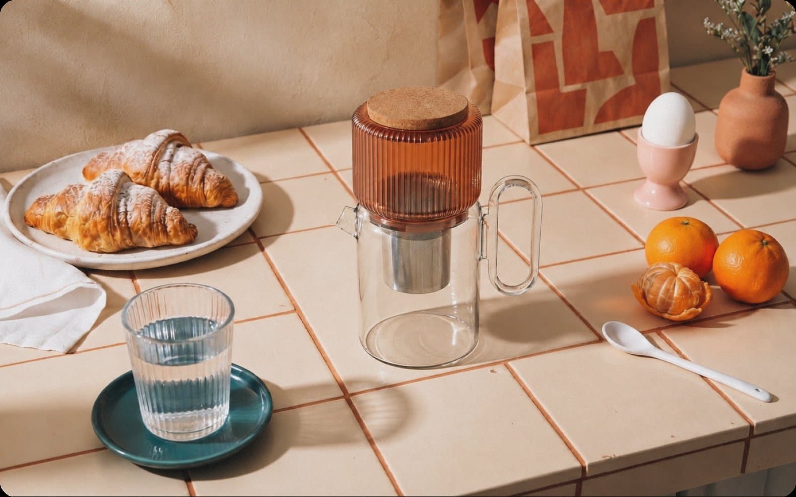 The omomi pitcher on a tiled breakfast table with croissants, oranges and a glass of water