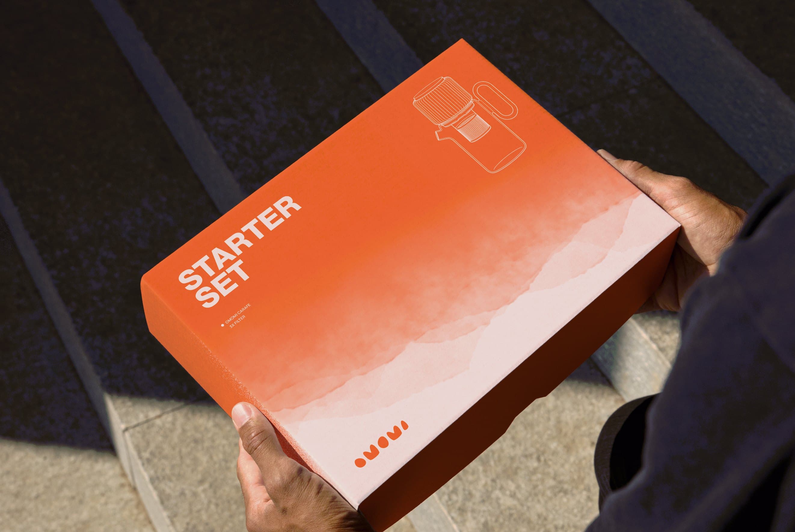 Hands holding the coral omomi Starter Set box